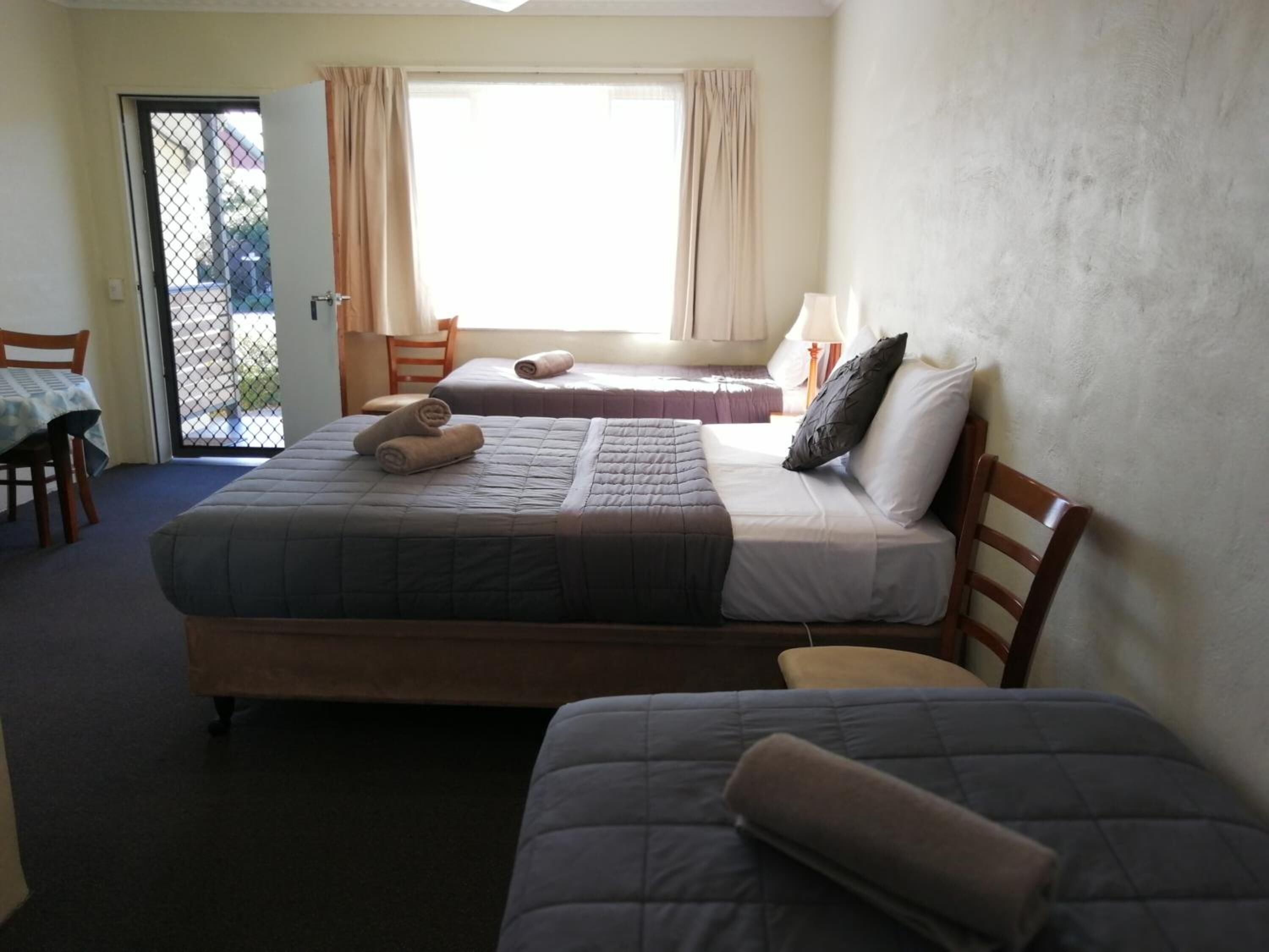 A hotel room with two beds, a table, chairs, and a window with curtains.