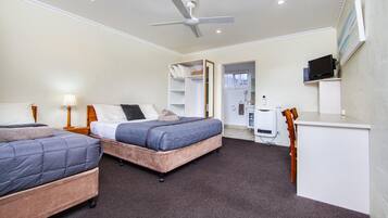 A hotel room with two beds, a desk, a chair, a TV, and a ceiling fan.