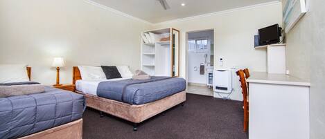 A hotel room with two beds, a desk, a chair, a TV, and a ceiling fan.