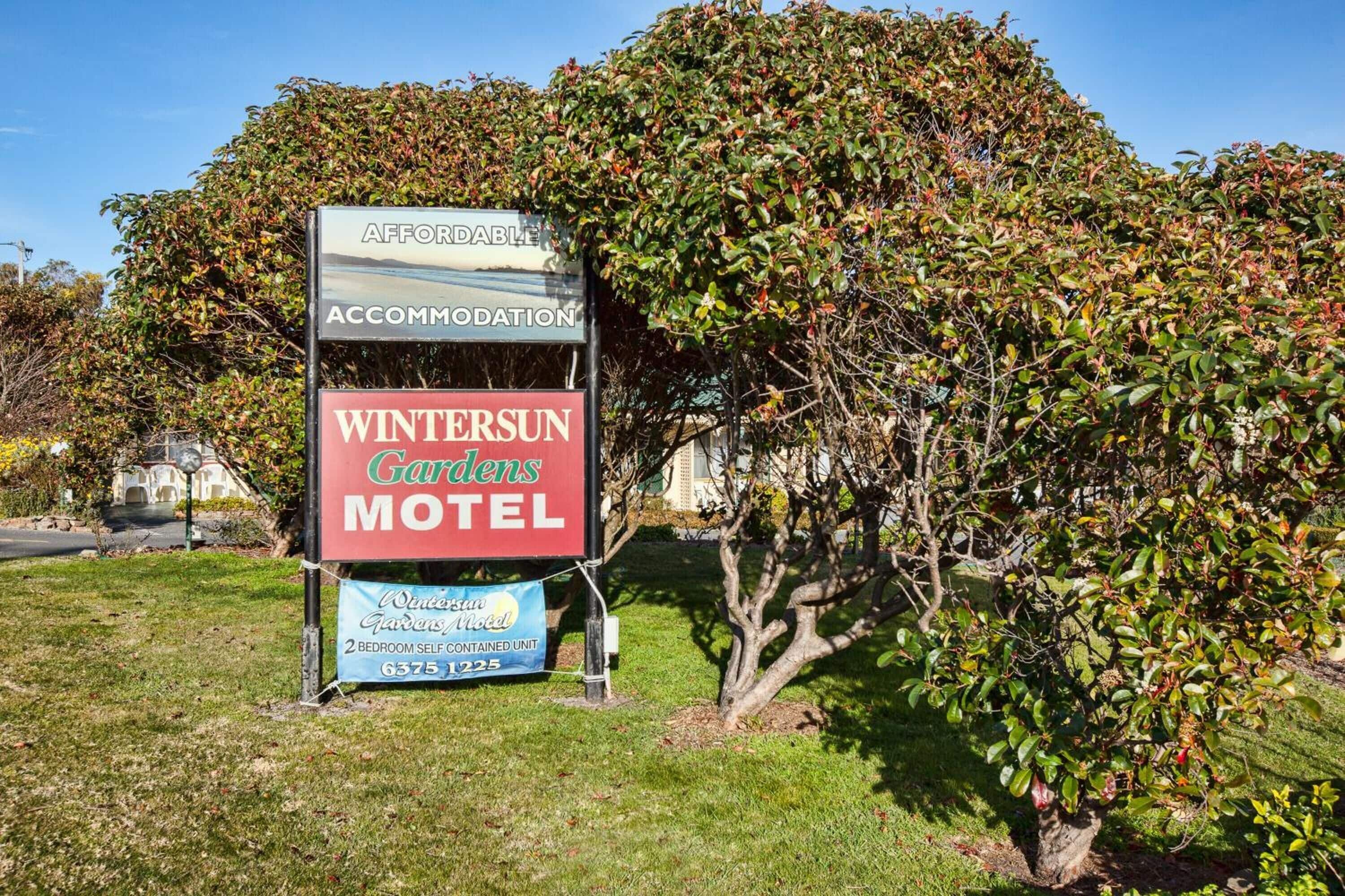 Une enseigne indiquant le « Wintersun Gardens Motel » et faisant la publicité d’un hébergement abordable, avec un appartement indépendant de deux chambres.