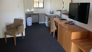 Una habitación de hotel compacta con kitchenette, televisor, escritorio y una silla.