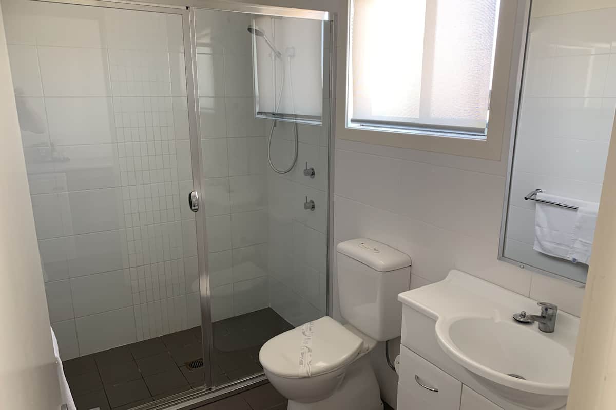 A bathroom with a glass-enclosed shower, a toilet, a sink, and a window.