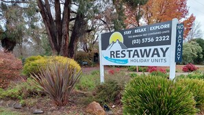 Placa de anúncio para as unidades de férias RESTAWAY, com ilustração de montanha e sol, localizada em Ovens River - Porepunkah, VIC.