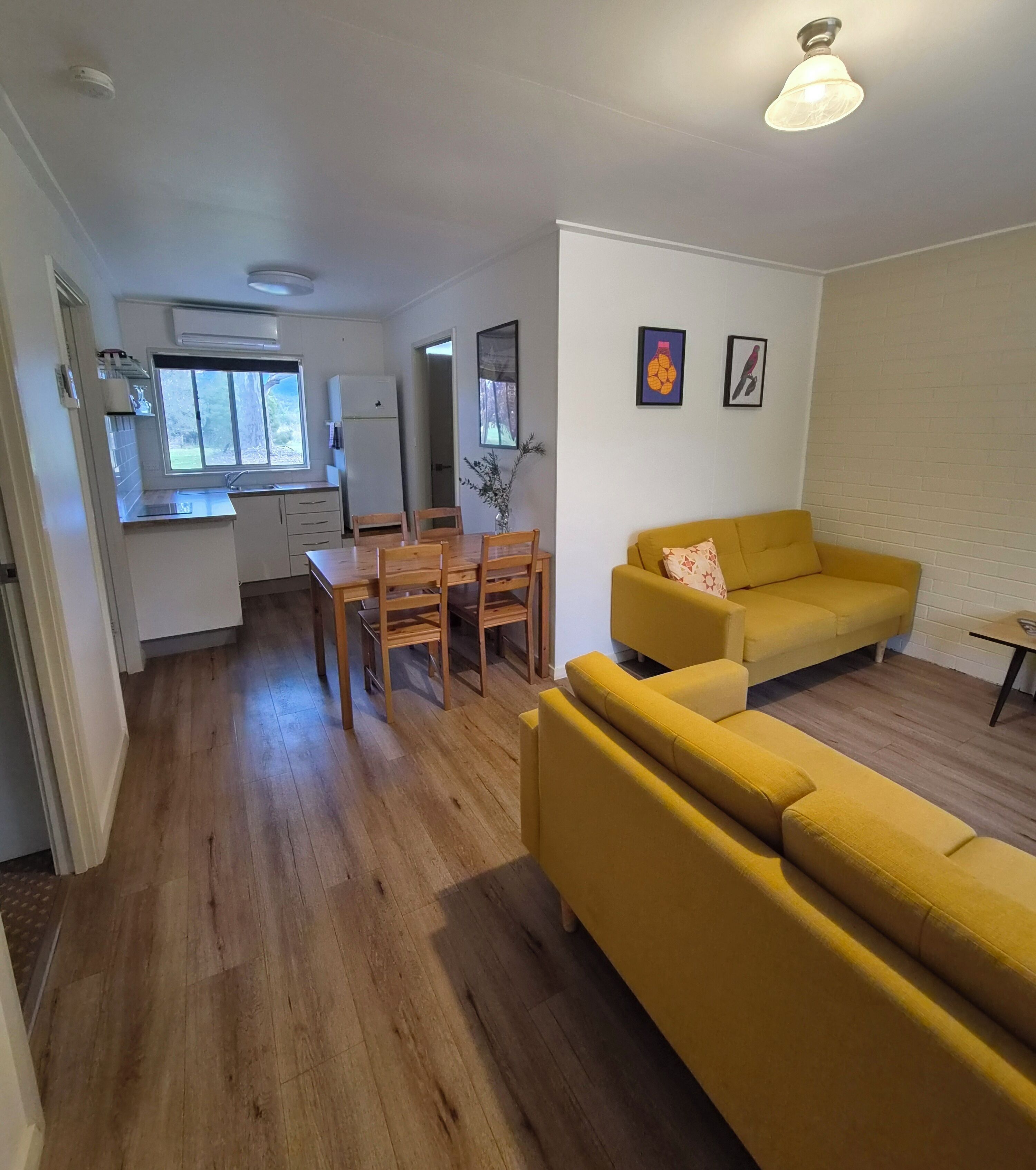 A living room with a yellow sofa, wooden dining table, and chairs.