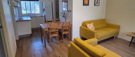A living room with a yellow sofa, wooden dining table, and chairs.