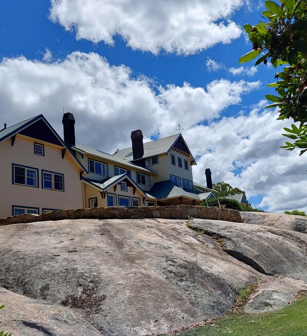 A large, multi-story house with a stone foundation, multiple chimneys, and a prominent roofline.