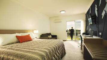 A hotel room with a bed, a desk, a chair, a sofa, and a sliding door leading to a balcony.