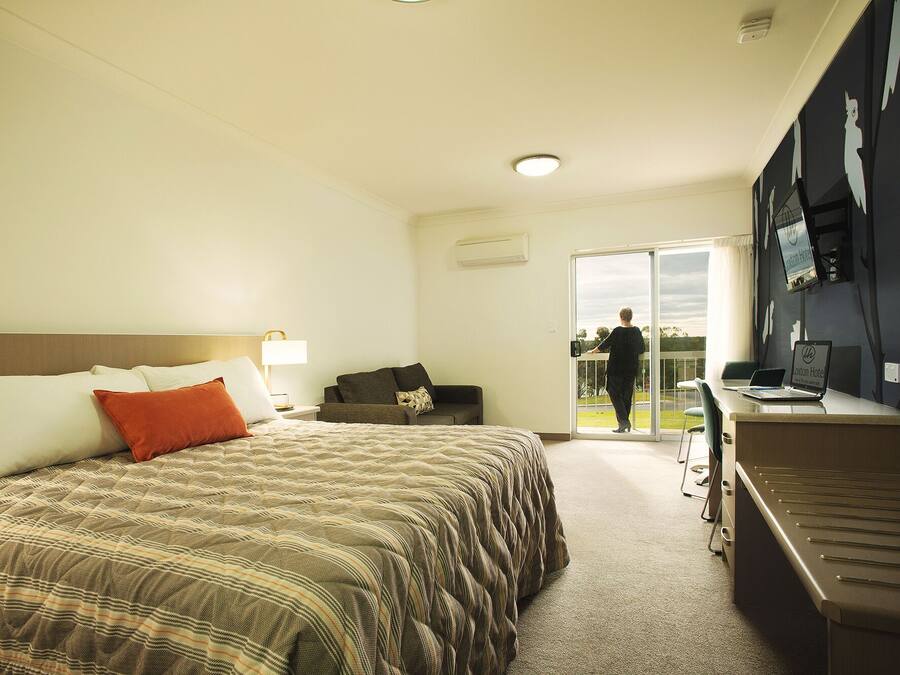 Une chambre d’hôtel comprenant un lit, un bureau, une chaise, un canapé et une porte coulissante donnant sur un balcon.