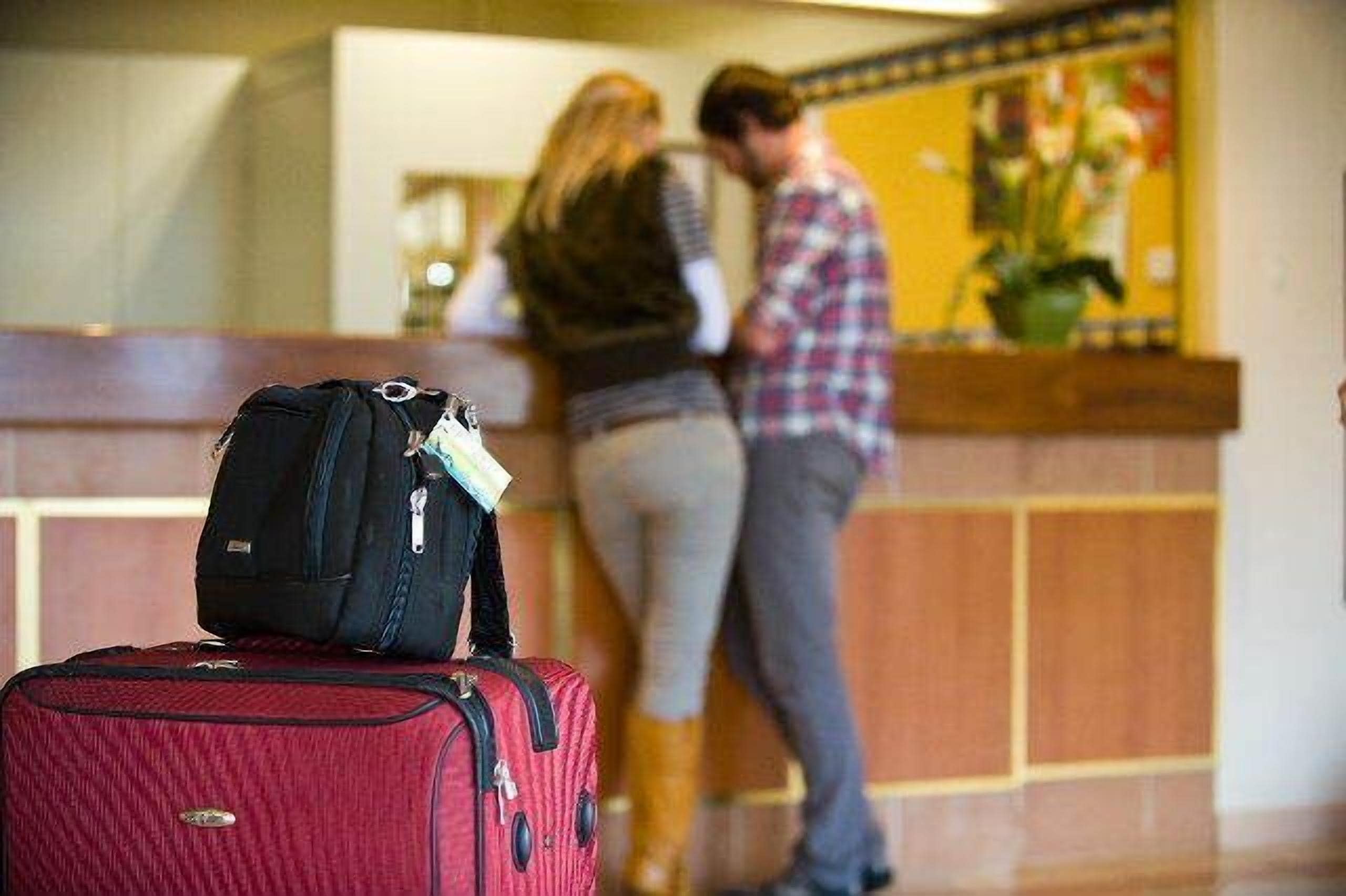 A reception area with a red suitcase and a black bag in the foreground.