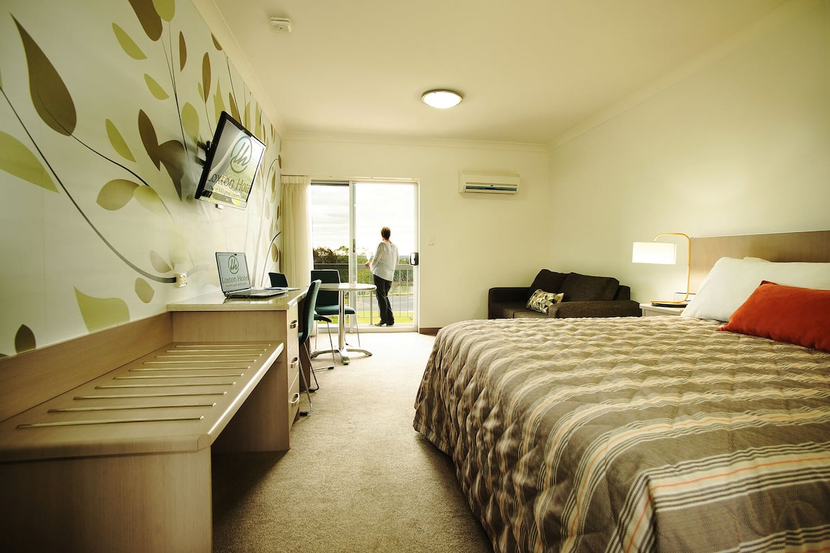 A hotel room with a bed, a desk, a chair, a TV, and a balcony.