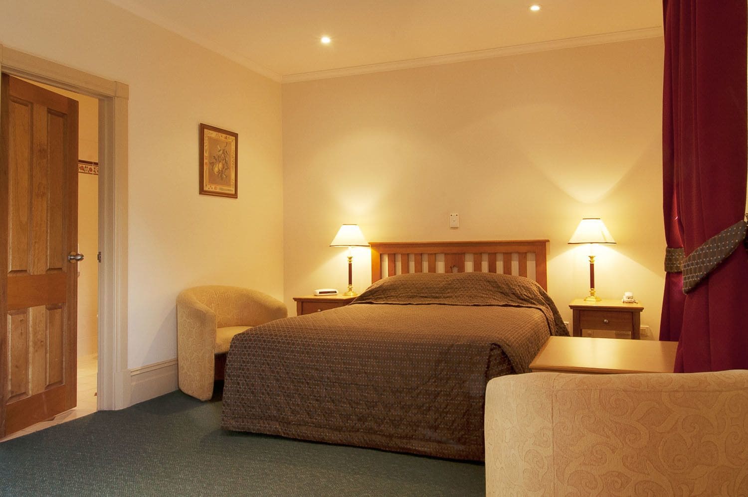 A hotel room with a bed, two bedside tables with lamps, a chair, and a door.