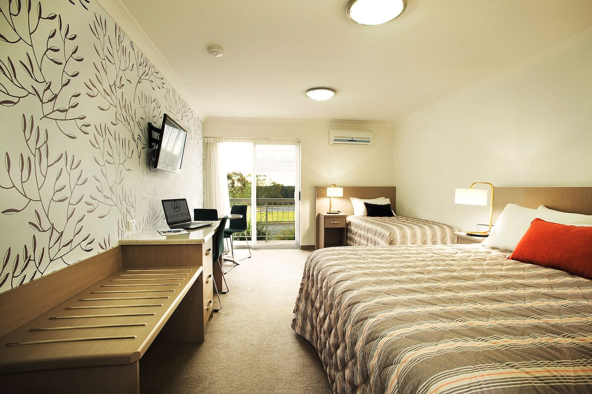 A hotel room with a bed, desk, and chair, a television, and a window with a view of greenery.