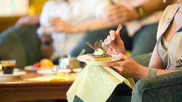 A person holding a plate with a dessert, seated at a table with a yellow tablecloth.