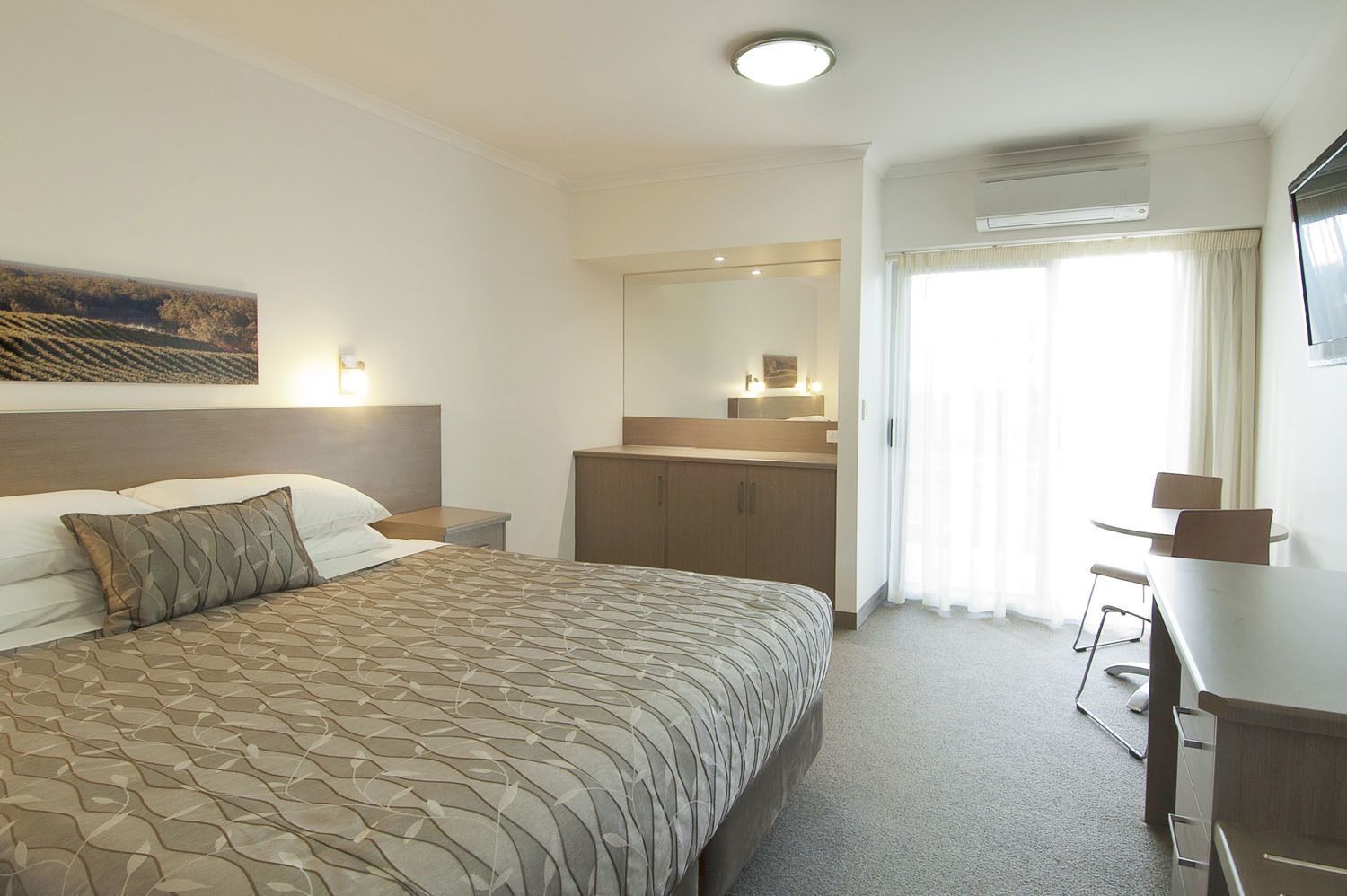 Hotellihuone, jossa on suuri sänky, työpöytä, peili ja ikkuna, jossa on verhot.