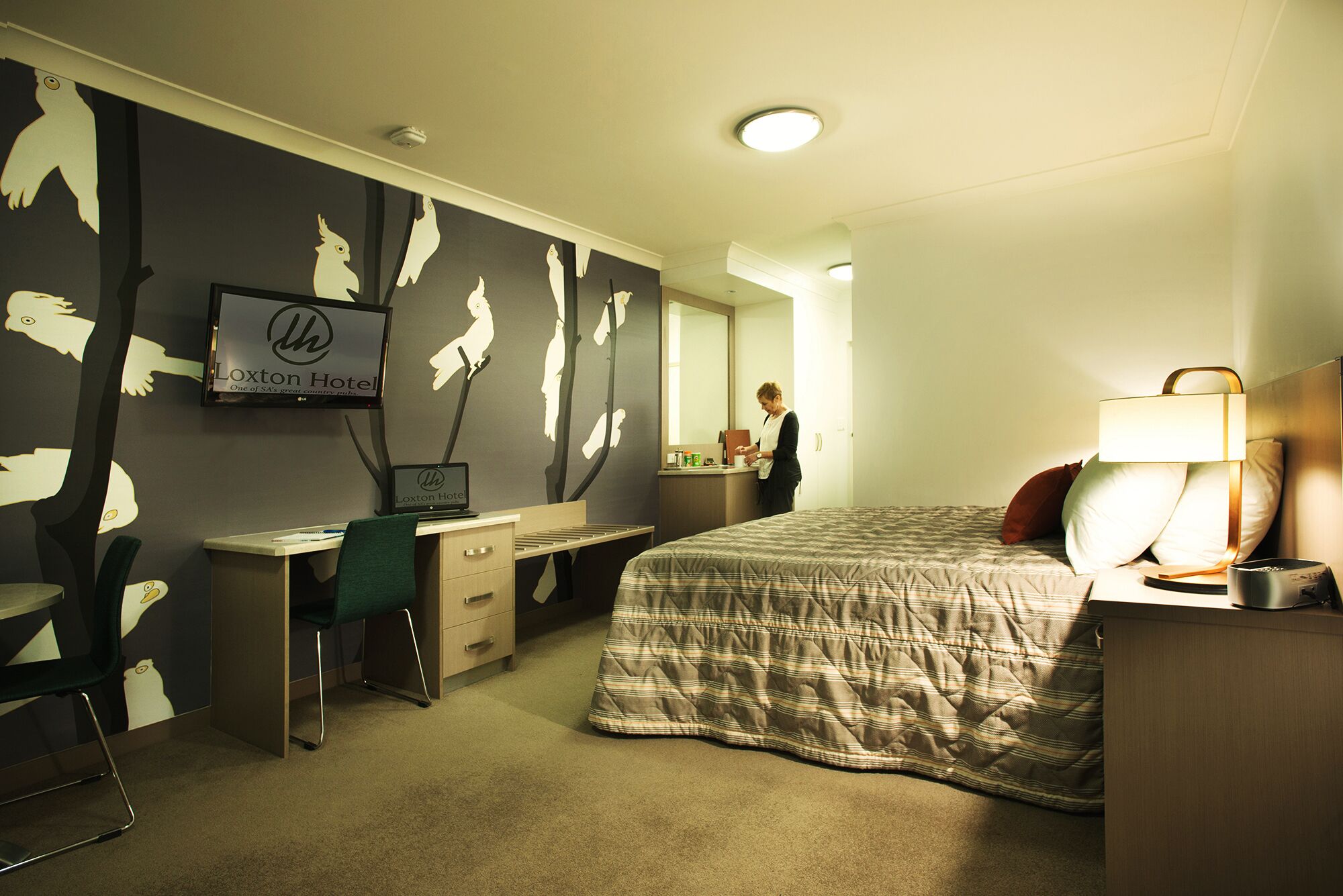 A hotel room with a bed, desk, chair, and a television.
