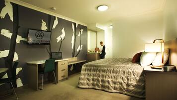A hotel room with a bed, desk, chair, and a television.