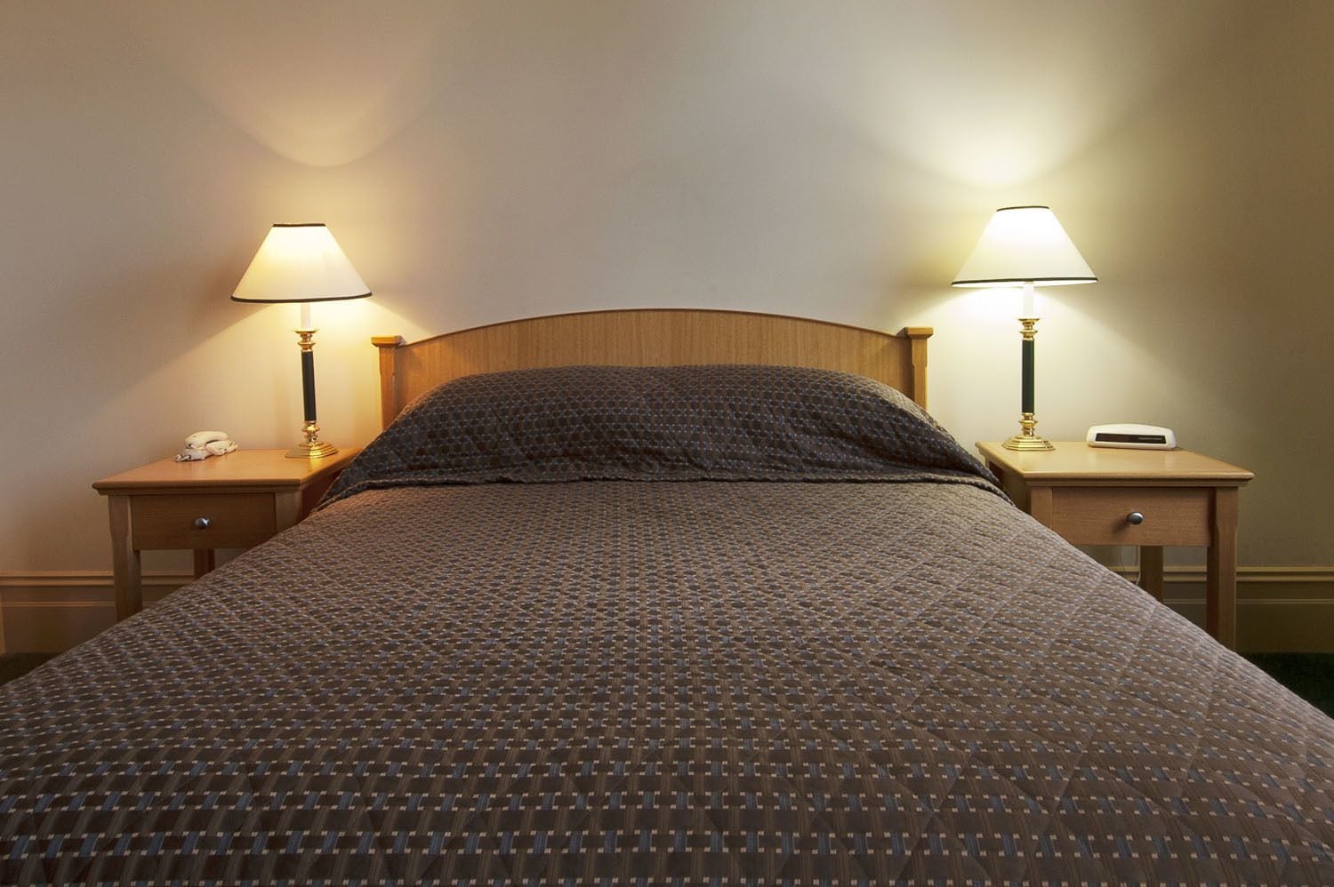 A neatly made bed with a patterned blanket, two bedside tables with lamps, and a phone on one of the tables.