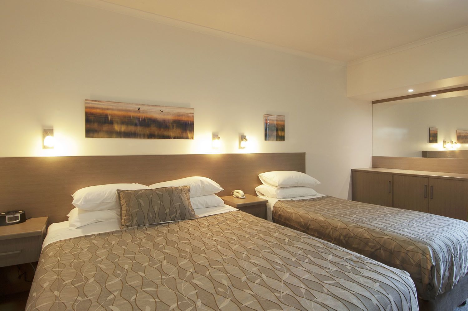 A hotel room with two beds, a nightstand with a phone, and a wall-mounted artwork.