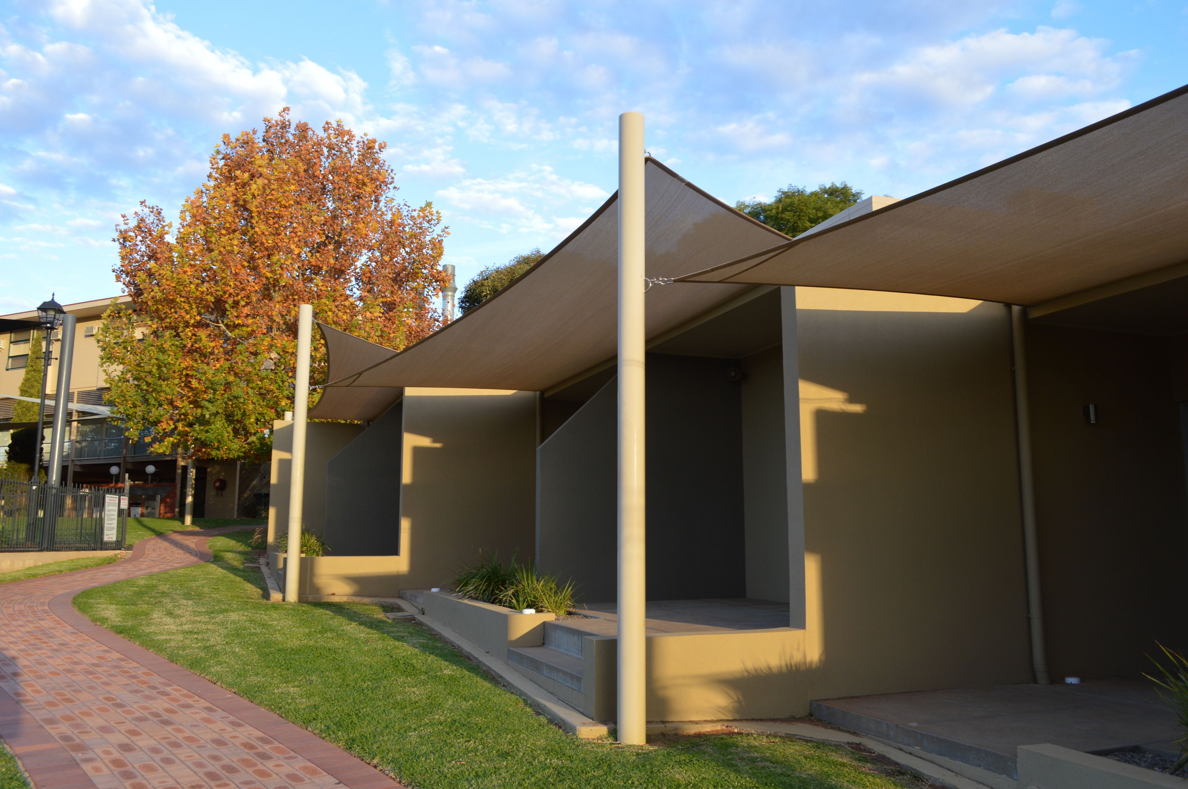 A modern building with a covered outdoor area, a brick pathway, and a tree with autumn leaves.