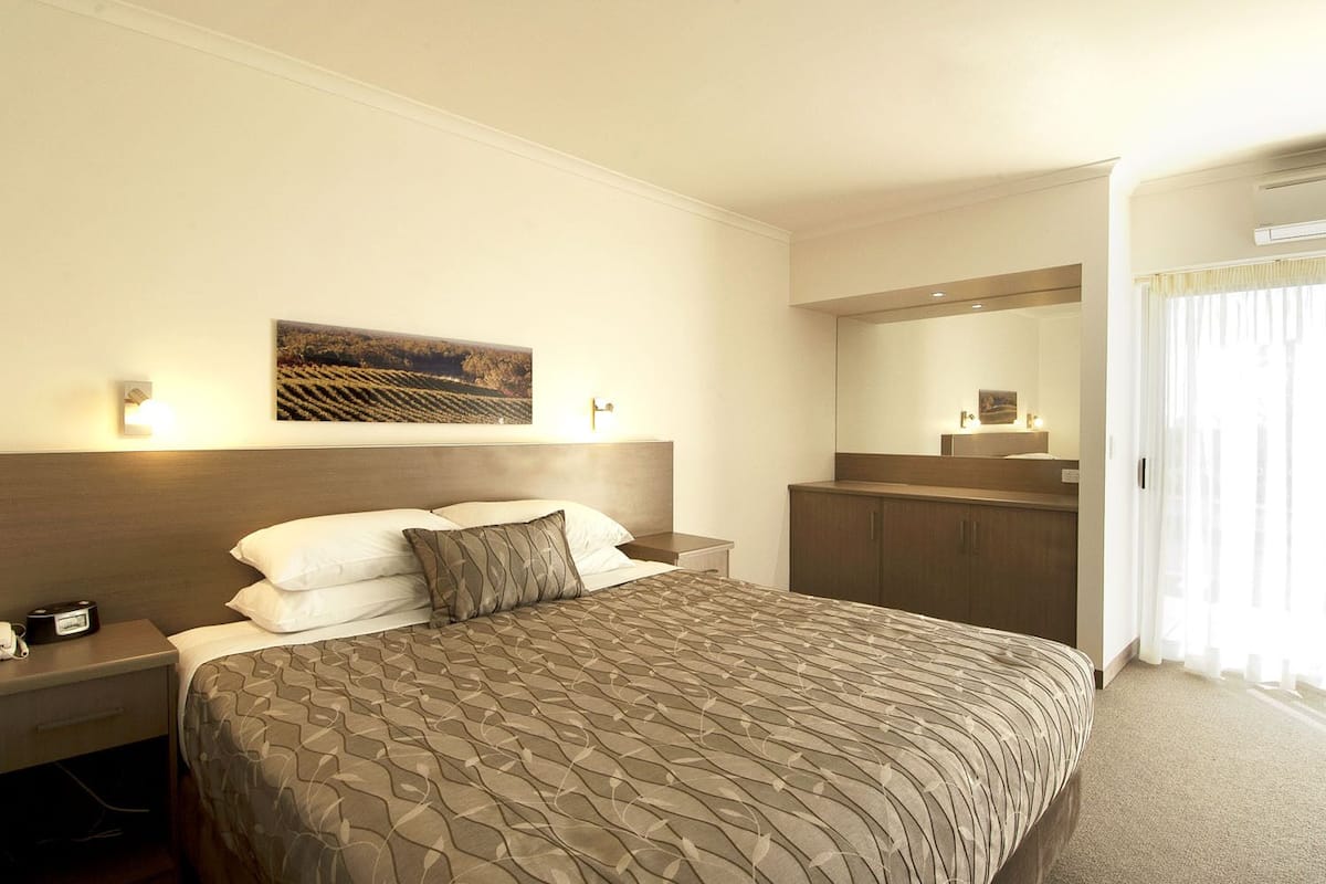A hotel room with a large bed, a nightstand with a lamp, a mirror, and a painting on the wall.