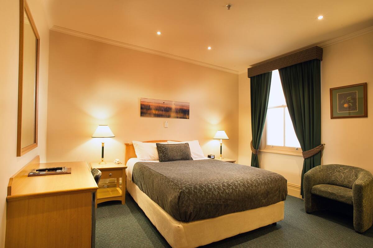 A hotel room with a large bed, two bedside lamps, a chair, and a painting on the wall.