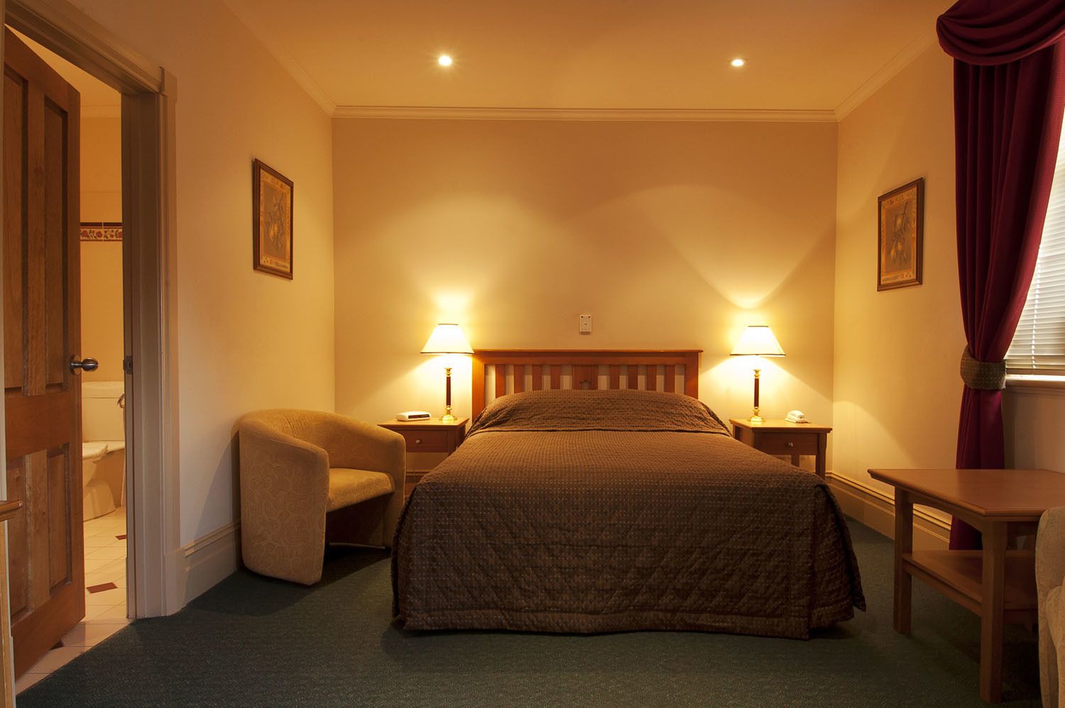 Una habitación de hotel con una cama, dos mesitas de noche con lámparas, una silla y una pequeña mesa.