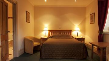 Una habitación de hotel con una cama, dos mesitas de noche con lámparas, una silla y una pequeña mesa.