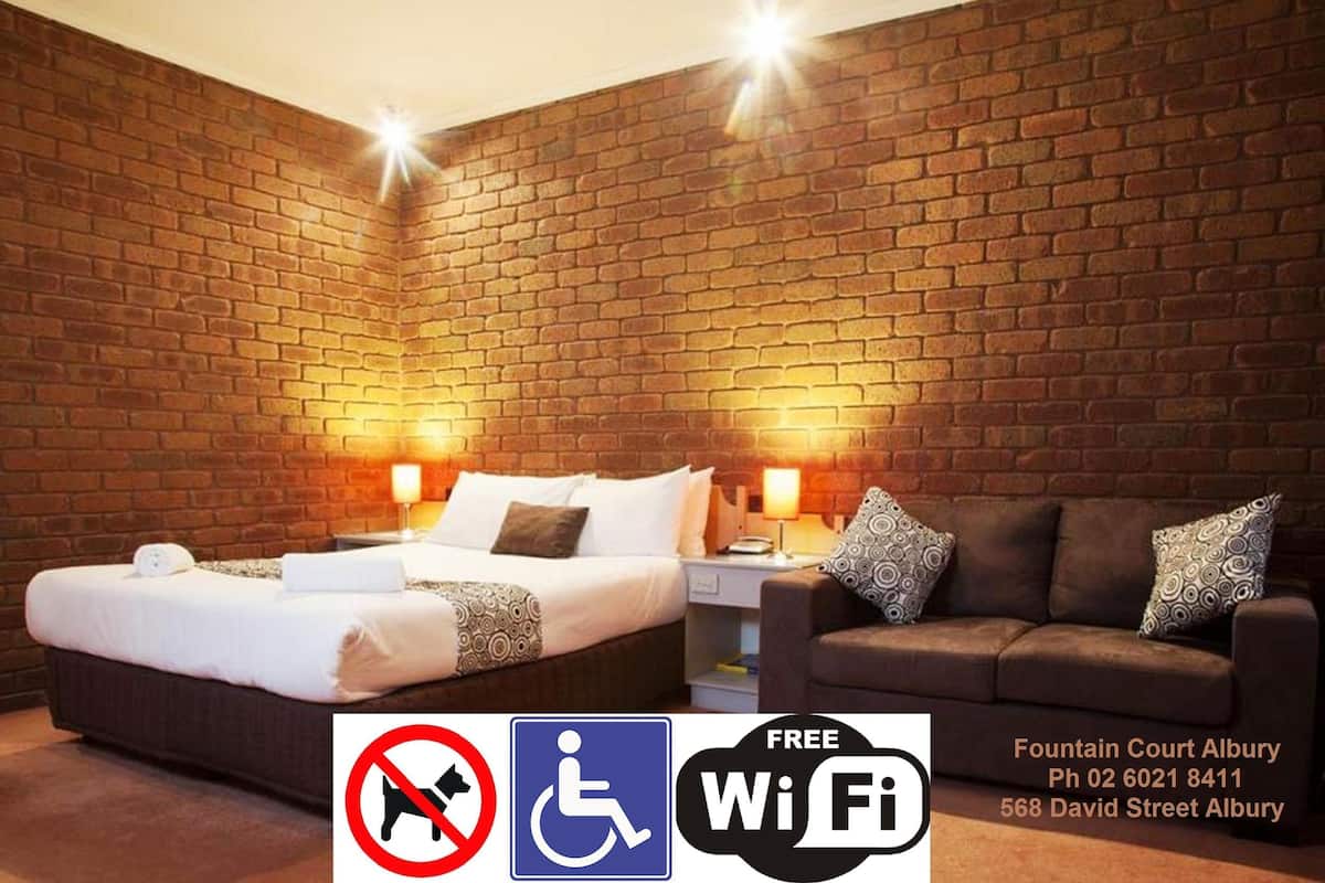 A hotel room with a brick wall, a bed, a sofa, and a nightstand. It includes a no smoking sign, a wheelchair accessibility symbol, and a free Wi-Fi sign.