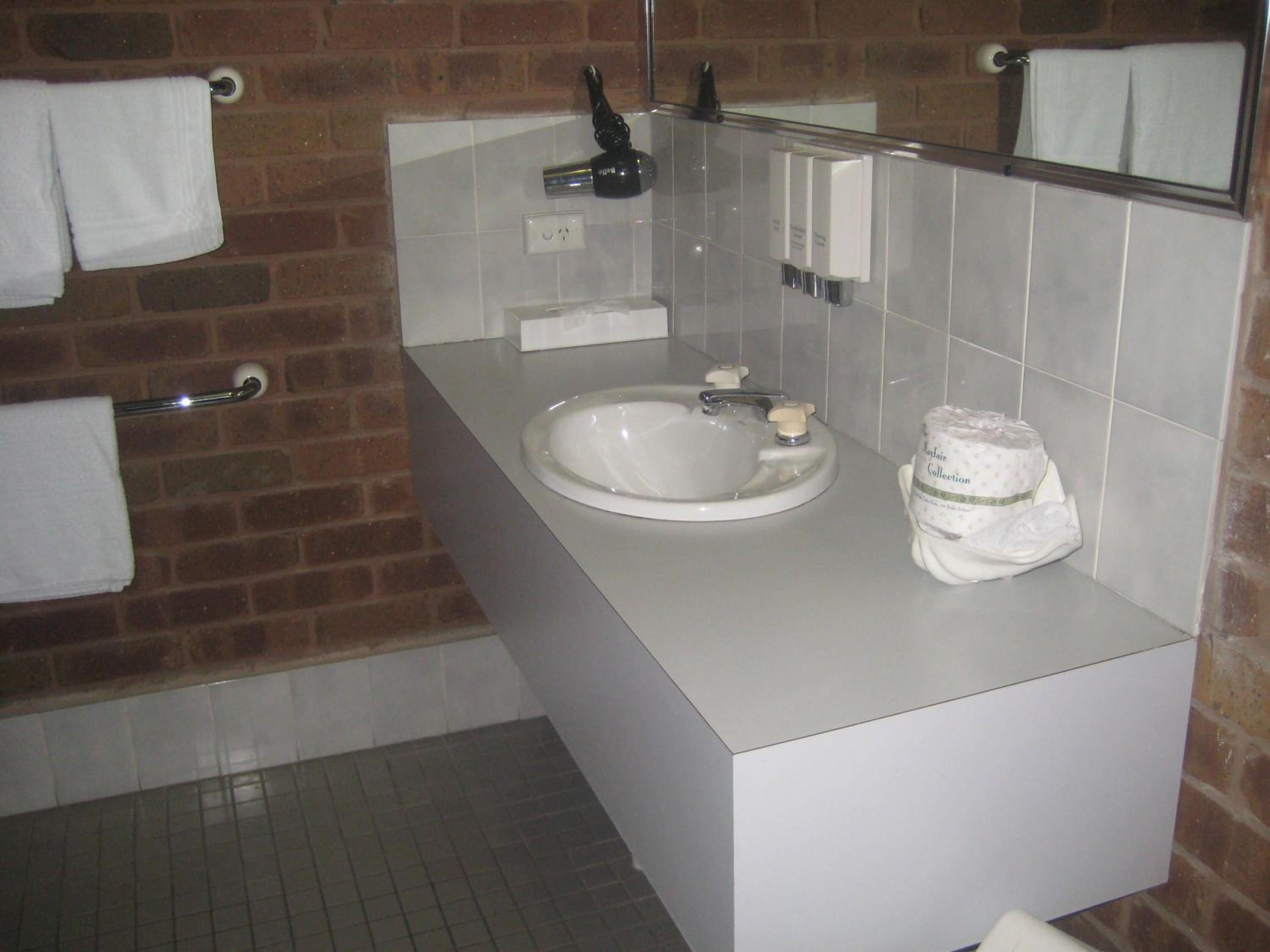 Un baño con lavamanos blanco, espejo y toallero.