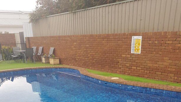 A swimming pool with blue tiles, surrounded by a brick wall and a metal fence. - Fountain Court Motor Inn Albury (Albury)