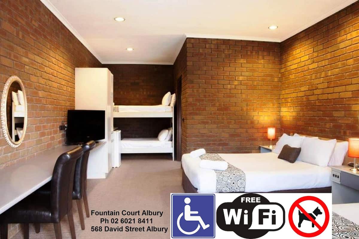 A hotel room with a brick wall, a bed, a desk with a chair, and a television.