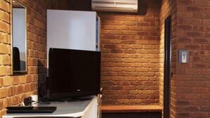 A room with a brick wall, a white refrigerator, a flat-screen TV, a wooden table, and a bench. - Fountain Court Motor Inn Albury (Albury)