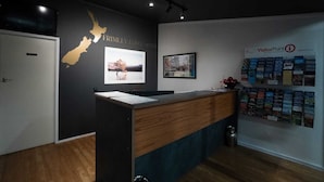 A reception desk with a map of New Zealand, framed pictures, and a wall with brochures. - Frimley Lodge Motel (Hastings)