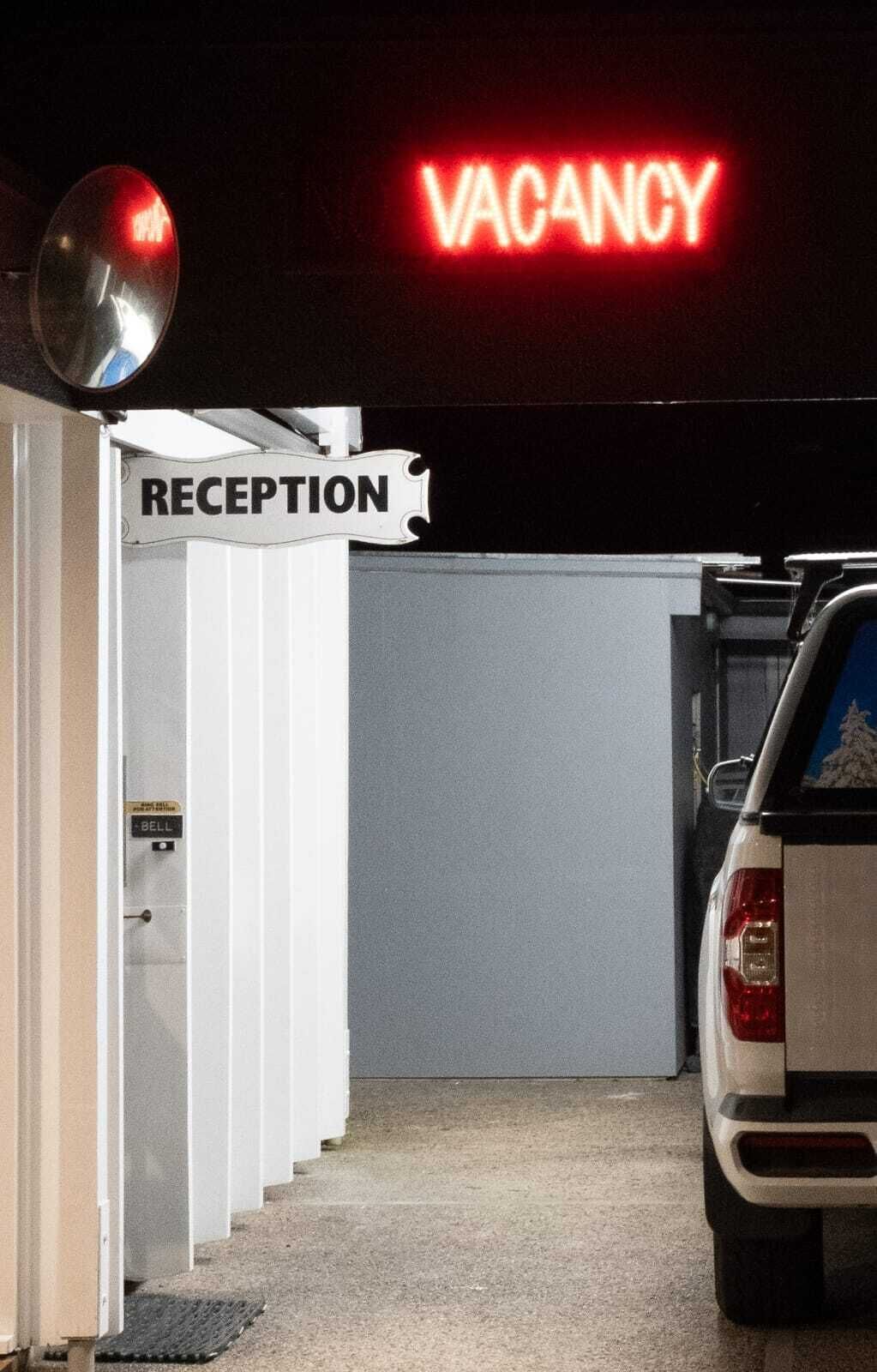 A reception area with a neon 'VACANCY' sign, a reception desk, and a car parked nearby.