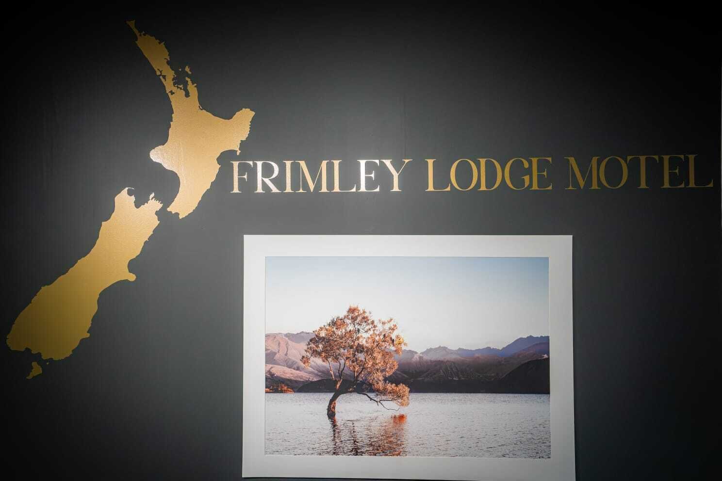 A map of New Zealand with the text "FRIMLEY LODGE MOTEL" and a photograph of a tree by a lake.