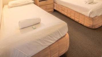 Habitación de hotel con dos camas, una mesita de noche de madera, una lámpara de pared y un ventanal con cortinas.
