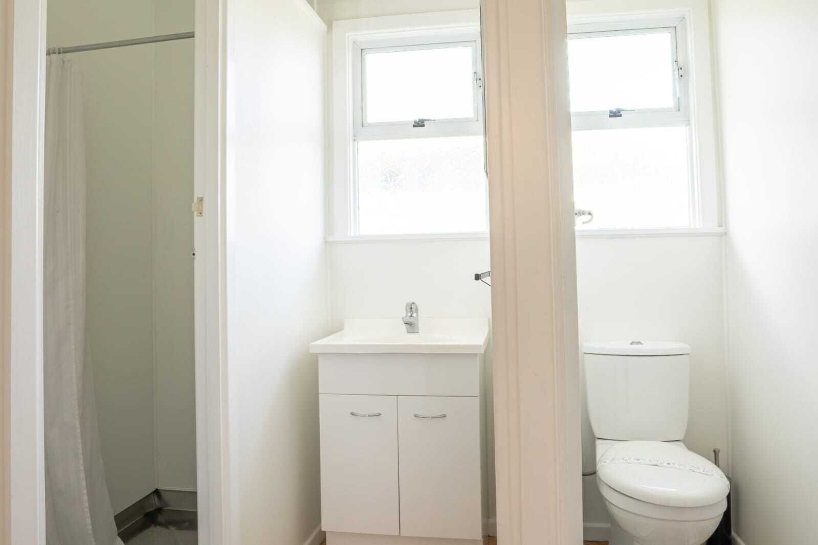 A small, white bathroom with a toilet, a sink, and a window above the sink.