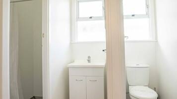 A small, white bathroom with a toilet, a sink, and a window above the sink.