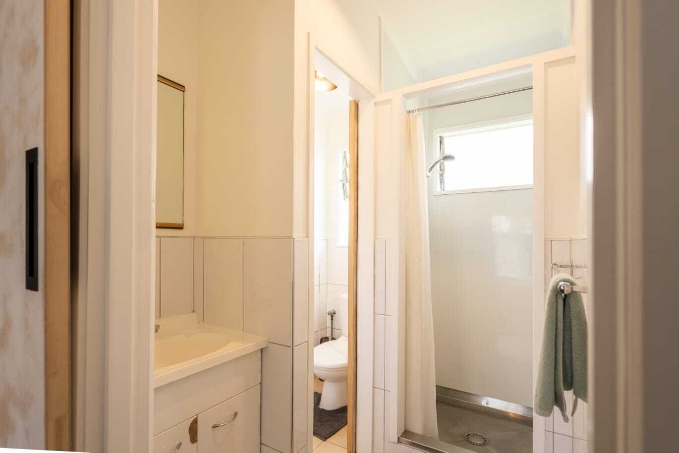 A narrow bathroom with a shower, a toilet, and a sink.