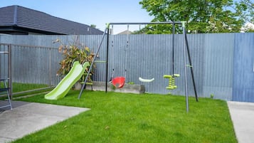 A backyard with a green slide, red swing, and yellow exercise equipment.
