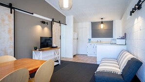 A compact living space with a dining area, kitchenette, and a seating area with a sofa. - Frimley Lodge Motel (Hastings)