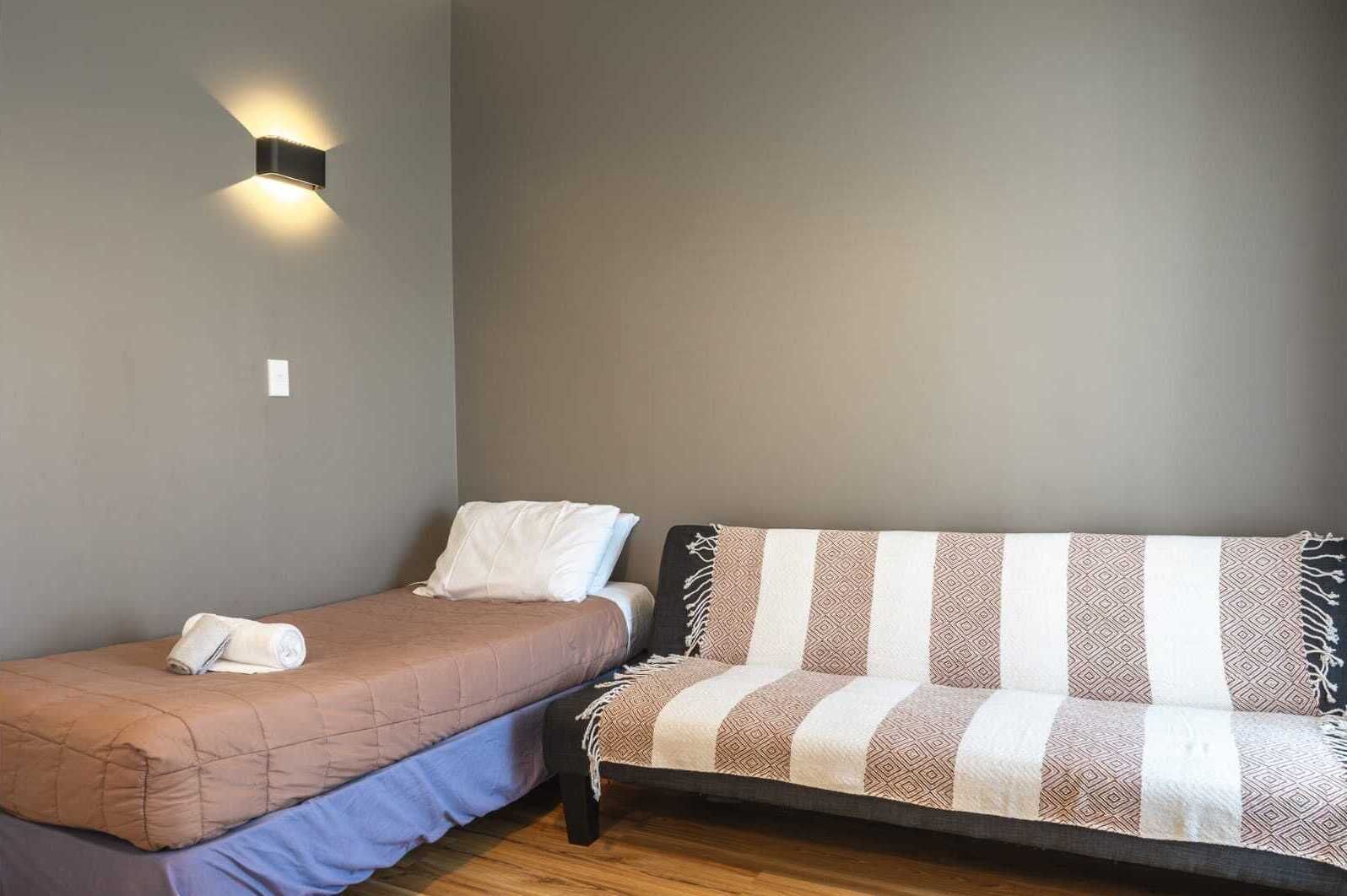 A bedroom with a single bed, a sofa, and a wall-mounted light fixture.