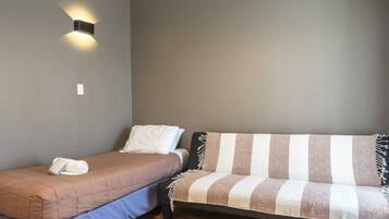 A bedroom with a single bed, a sofa, and a wall-mounted light fixture.