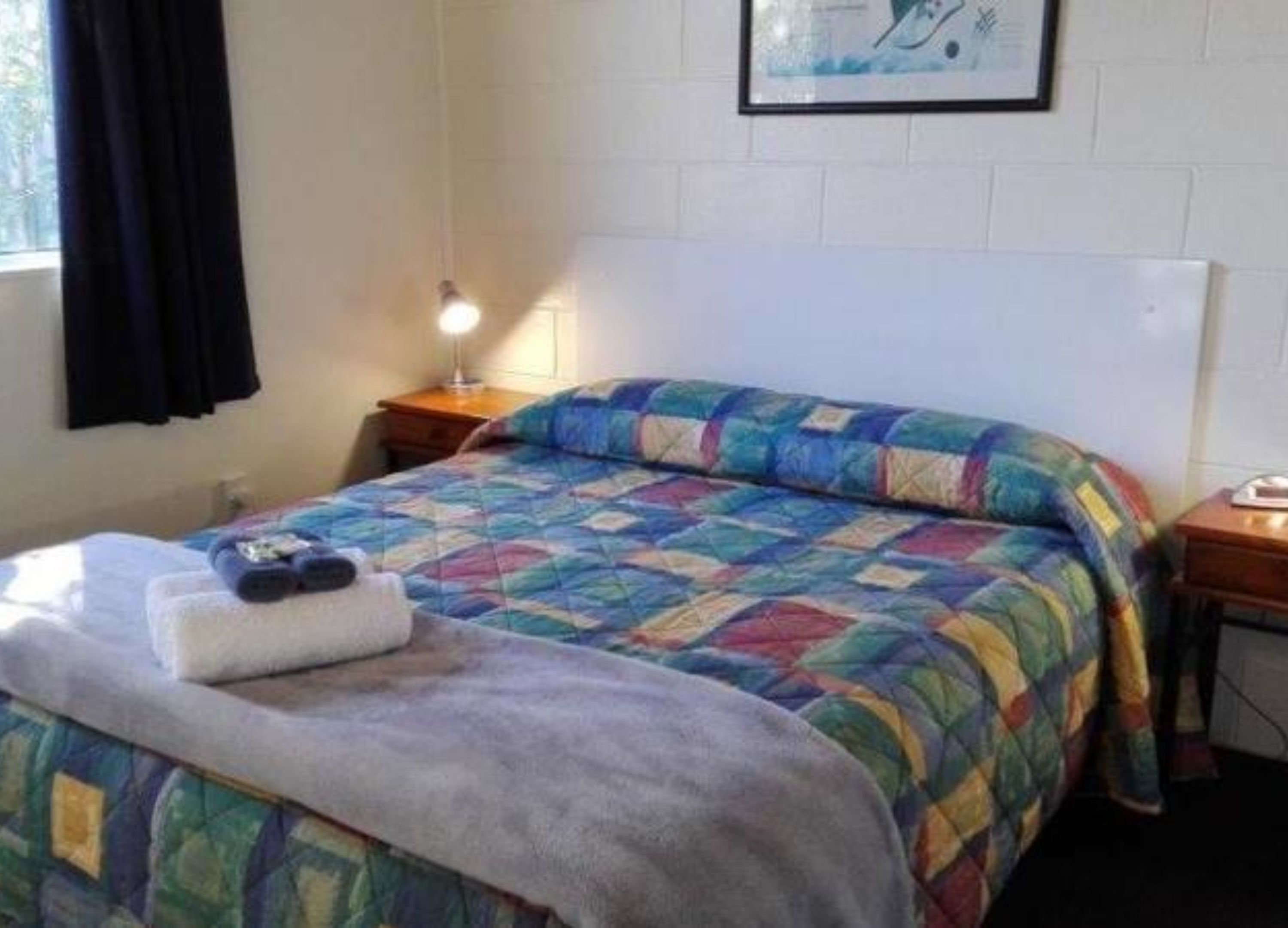 Una cama individual con un edredón colorido, una lámpara de noche y un cuadro en la pared.
