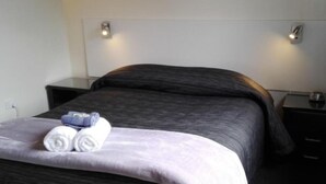 A neatly made bed with a dark headboard and two bedside tables, one with a lamp.
