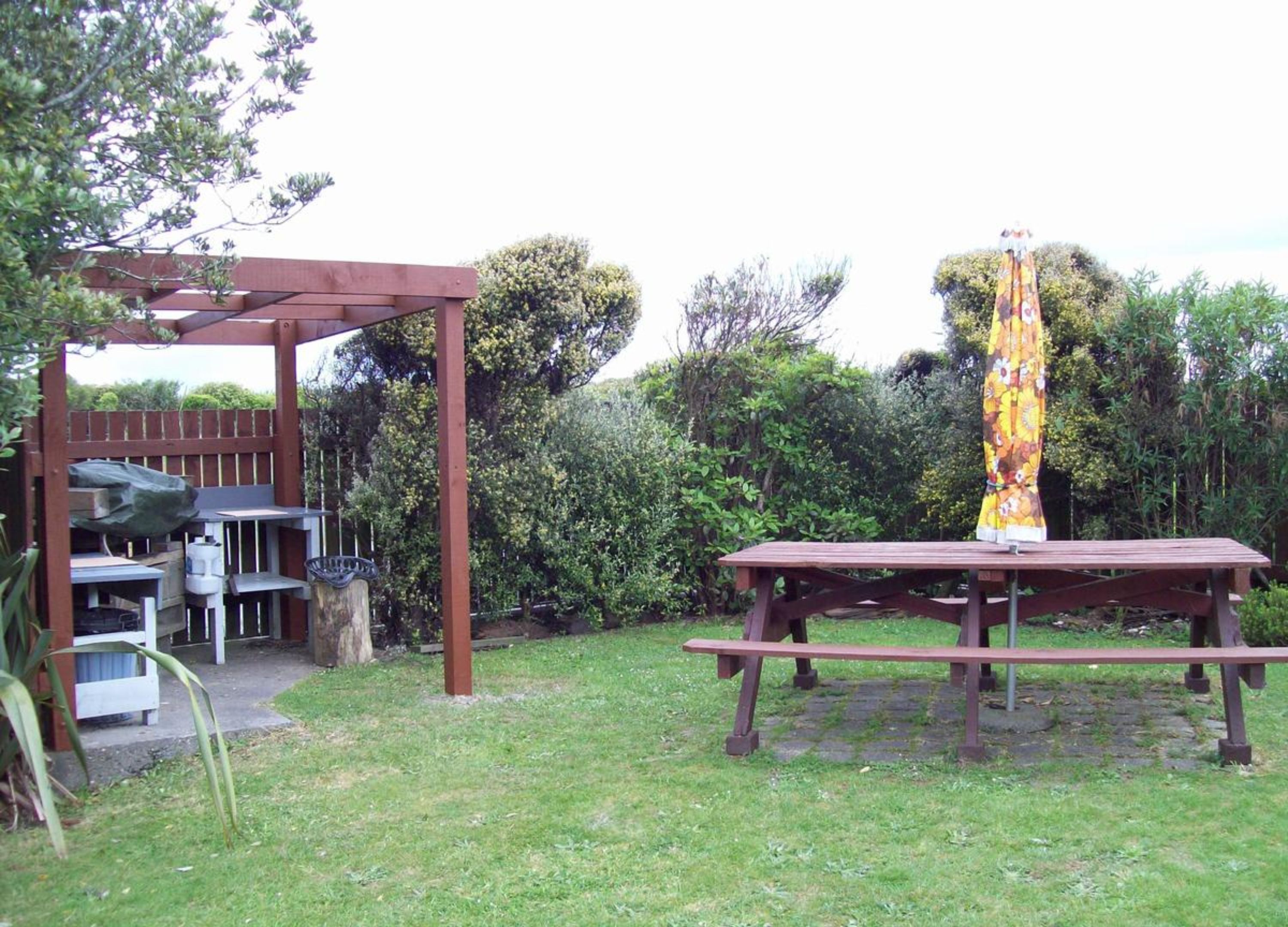 Una pérgola de madera con zona de barbacoa, una mesa de picnic y un paraguas cubierto.