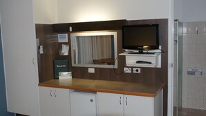 Habitación de hotel con mostrador de madera, televisión, espejo, una mesita y armarios.