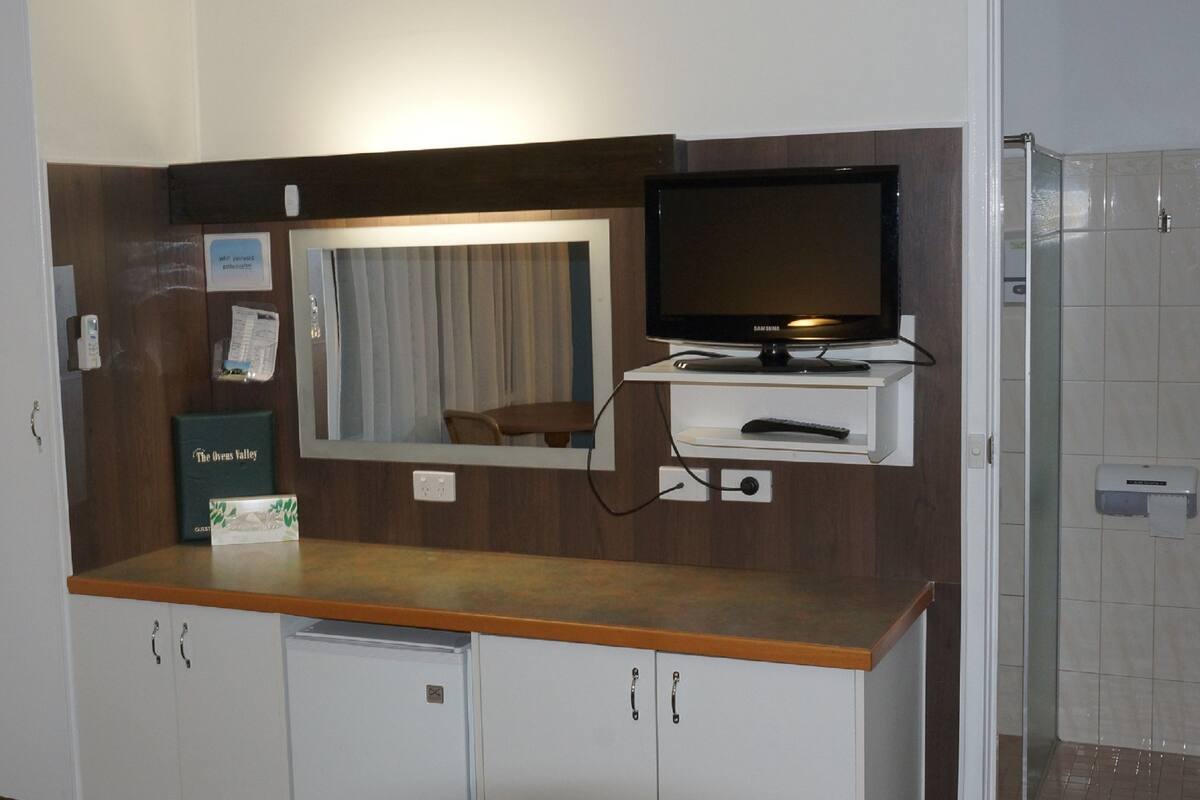 A hotel room with a wooden counter, a television, a mirror, a small table, and cabinets.
