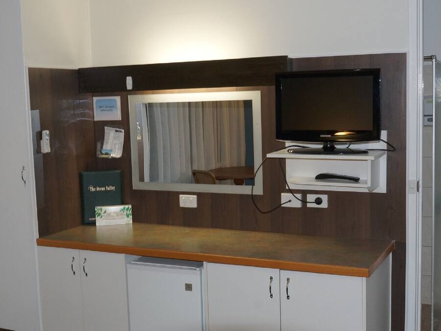 A hotel room with a wooden counter, a television, a mirror, a small table, and cabinets.