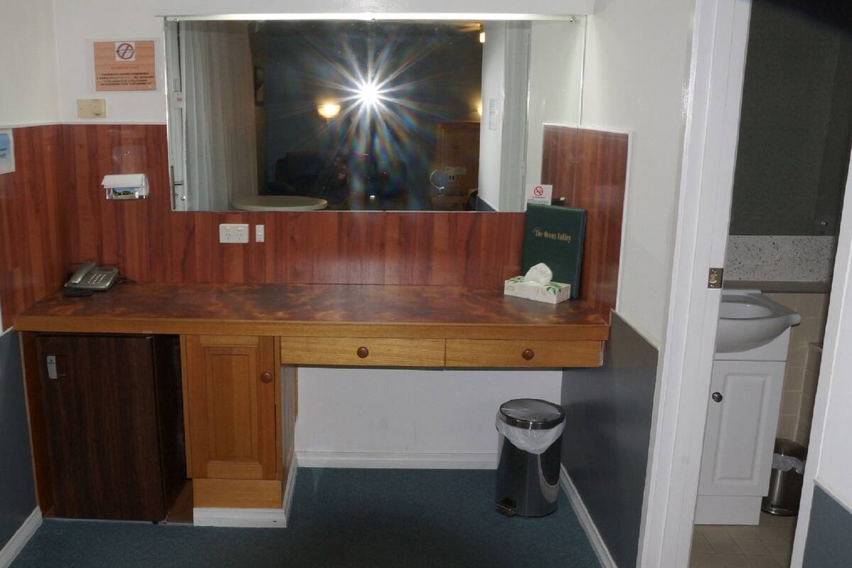 A small bathroom with a wooden vanity, a mirror, a sink, and a trash can.